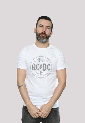 Weißes Baumwoll-T-Shirt mit einem runden Grafikdruck von "AC/DC" mit Blitzen und Text, getragen mit dunklen Jeans.