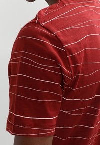 Punainen lyhythihainen paita, jossa on valkoisia vaakaraitoja, pyöreä pääntie ja pehmeä rakenne, suunniteltu mukavuutta ja rentoa käyttöä varten.