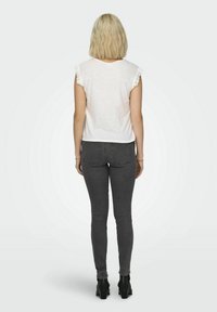 Haut blanc à manches courtes avec bordure en dentelle, associé à un jean slim gris foncé et des bottes à talons noires, vu de l'arrière.