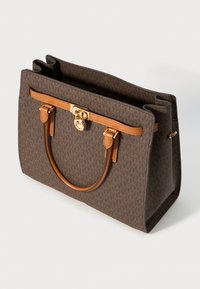 Sac fourre-tout en monogramme brun avec des poignées et des finitions en cuir beige, détail en métal doré en forme de serrure et un design structuré à ouverture supérieure.