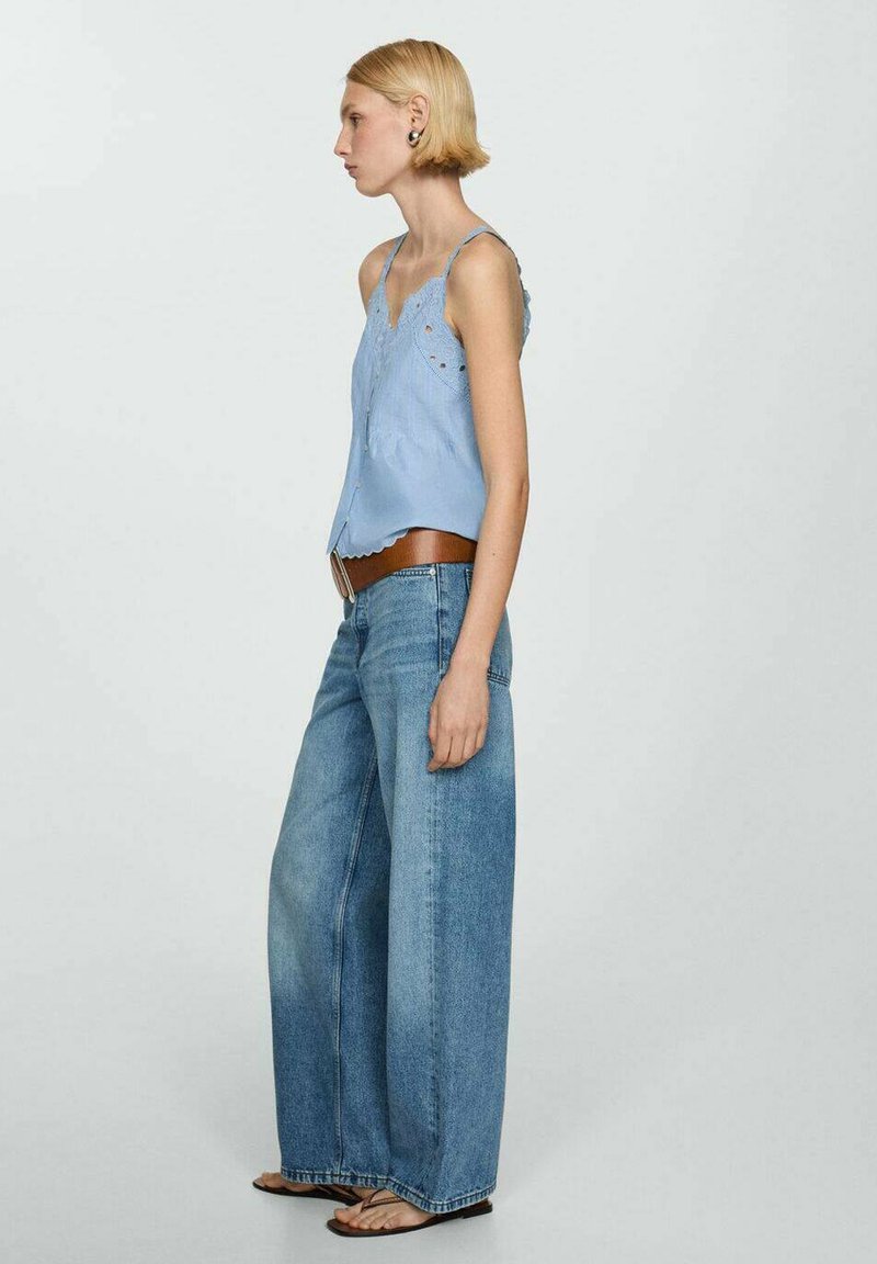 Jasnoniebieska bawełniana bluzka z koronkowymi detalami i guzikami, zestawiona z szerokimi niebieskimi dżinsami i brązowym skórzanym paskiem. Teksturowana tkanina.