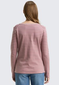Top de manga larga a rayas rosas, hecho de una tela suave, con escote redondeado, corte relajado y dobladillo ligeramente redondeado, combinado con unos jeans de color azul claro.