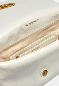 Borsa a mano bianca in finta pelle con una texture liscia, accessori dorati e tasca interna. Presenta il marchio "LIU JO LAPUFFY" sulla fodera.