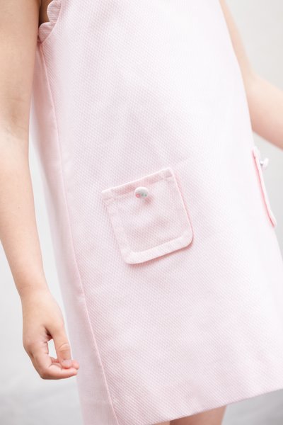 Φουξ ροζ φόρεμα με υφή υφάσματος, που διαθέτει τσέπη με διακοσμητικό κουμπί και βολάν στις μασχάλες. Απλός και λειτουργικός σχεδιασμός.