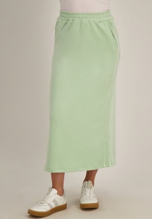 Lichtgroene midirok met elastische tailleband en zijzakken, gecombineerd met witte sneakers met rubberen zolen.