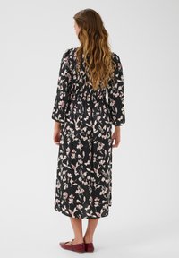 Rochie neagră cu flori, cu mâneci lungi, bust strâns și modele cu flori roz. Material neted și design până la gleznă. Asortată cu pantofi plată burgundy.