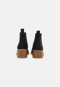 Bottines noires en daim avec une finition texturée, bout rond et talon en bois empilé. Équipées de languettes à l'arrière pour un enfilage facile.