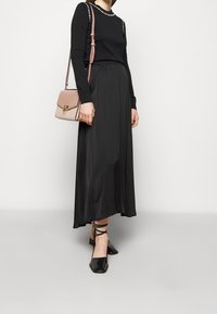 Schwarz langärmliges Shirt mit weißen Nähten, kombiniert mit einem schwarzen satin Maxi-Rock. Schwarze flache Schuhe mit Knöchelriemen und einer rosa Umhängetasche.