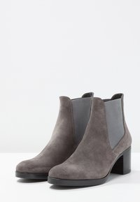 Stivaletti alla caviglia grigi in suede con pannelli elastici laterali e tacco impilato. Texture liscia con dettagli di cucitura a contrasto. Design classico e versatile.