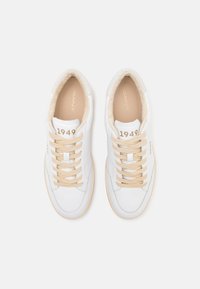 Weiße Leder-Sneaker mit beigen Schnürsenkeln, weichem beige Innenfutter und "1949" auf der Zunge, von oben auf einem weißen Hintergrund betrachtet.