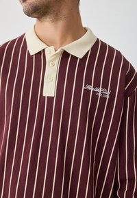 Bordo dryžuotas polo marškinėliai su kremine apykakle, turintys tris mygtukus ir išsiuvinėtą tekstą "Sveikatos klubas EST. 1993" baltai.