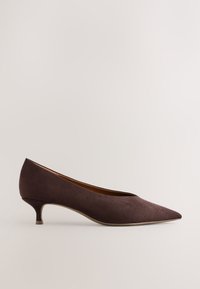 Chaussure en daim brun foncé à bout pointu, talon kitten fin et côtés échancrés sur un fond clair uni.