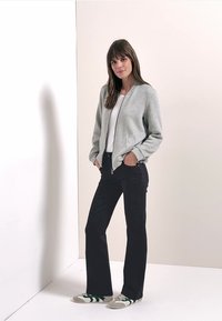 Ljusgrå zip-up sweatshirt med ribbad krage, kombinerad med svarta utsvängda jeans och grå sneakers med gröna ränder.