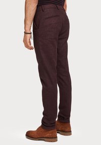 Bordowe spodnie o fakturowanym wykończeniu, z tylną kieszenią, połączone z brązowymi zamszowymi butami sznurowanymi. Prosty fason z nogawkami o prostym kroju.