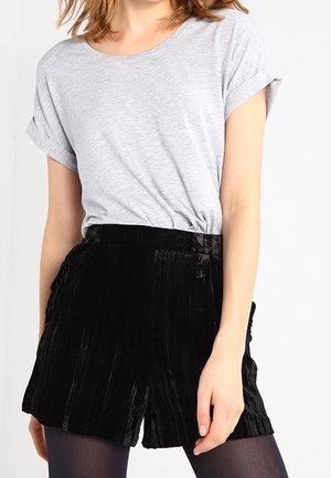 Femme portant un t-shirt à manches courtes gris clair, rentré dans un short en velours noir taille haute avec des collants noirs.