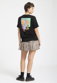 Camiseta negra con gráfico de gato colorido en la parte posterior, combinada con una falda plisada de estampado de leopardo y zapatos negros con cordones.