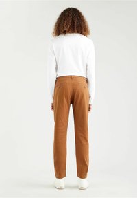 Bruna bomullsbukser med en avsmalnande passform, bakfickor och en slät yta, i kombination med en vit långärmad skjorta och vita skor.