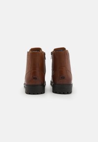 Brūni ādas potīšu zābaki ar gludu tekstūru, ar sānu rāvējslēdzēju, izturīgu melnu gumijas zoli un minimālu zīmola detaļu.