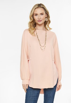 Maglietta a maniche lunghe color pesca con un fit rilassato, pannelli laterali testurizzati e orlo arrotondato. Abbinata a una collana di perline a strati e denim.