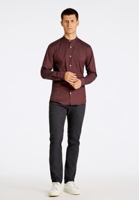 Bordeaux langharige shirt met een staande kraag en voorknoopjes, gecombineerd met zwarte broeken en witte sneakers. Gladde stofstructuur.