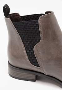 Bottine en cuir gris avec panneaux latéraux élastiqués noirs en tissu tressé, un petit talon empilé et une couture contrastante le long des coutures.