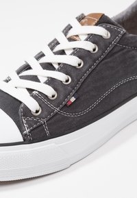 Šedé plátěné tenisky s bílými tkaničkami, gumovou špičkou a černou gumovou podrážkou. Obsahují hnědou koženou akcentu a prošívané detaily.