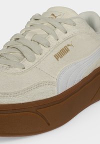 Бежова кец с велур на Puma с бяла ивица, кафяво лого на Puma, дебела кафява подметка и бежови връзки.