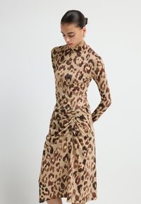 Abito aderente a maniche lunghe con stampa leopardata, avente una base beige e dettagli marroni; presenta morbide pieghe lateralmente.