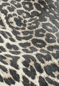 Tissu avec un motif léopard mettant en avant des tons noirs et beiges, présentant une surface texturée avec un motif distinct et des couleurs contrastées.