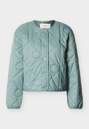 Jasnoniebieska pikowana kurtka wykonana z gładkiej tkaniny, z okrągłym dekoltem, zapięciem na zatrzaski oraz ukośnym przeszyciem z okrągłymi akcentami.