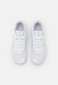 White athletic shoes with mesh upper, textured sole, and light green accents. Features traditional lacing and branded logo.