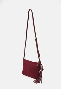 Sac en daim bordeaux à bandoulière avec une longue sangle réglable, doté d'une fermeture à rabat et d'un détail de gland sur le côté.