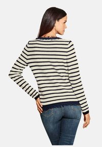 Gestreepte trui in crème en marineblauw, met een rafelige zoom en manchetten, in een aansluitende pasvorm met lange mouwen. Gekleed over denim jeans.
