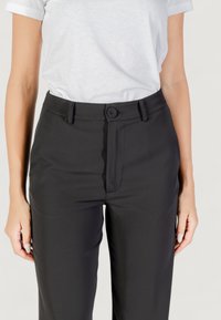 Pantaloni neri su misura con una texture liscia, chiusura con bottone, passanti per la cintura e un design a gamba dritta, abbinati a una t-shirt bianca aderente.