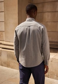 Grijze overhemden met een afgeronde zoom, lange mouwen en een rugplooitje, gecombineerd met marineblauwe streepjesbroek. Glad materiaal, casual ontwerp.