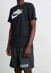 Camiseta de algodón negra con un gráfico colorido de "Just Do It", combinada con pantalones cortos deportivos negros que presentan un logo blanco de "JORDAN".
