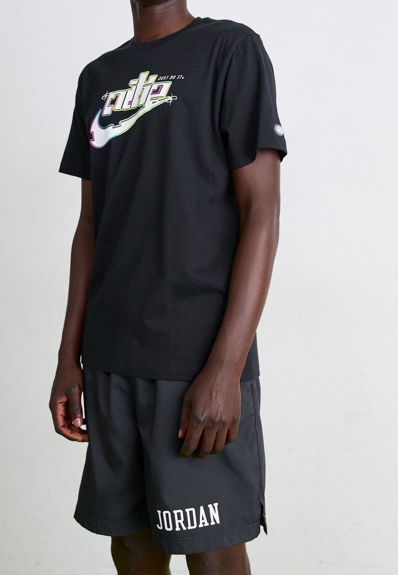 Camiseta de algodón negra con un gráfico colorido de "Just Do It", combinada con pantalones cortos deportivos negros que presentan un logo blanco de "JORDAN".