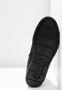 Semelle en caoutchouc noire d'une chaussure avec des rainures profondes pour l'adhérence et le nom de marque embossé "ecco" près du talon.