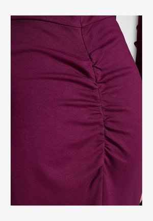 Gros plan sur un vêtement en tissu violet avec un détail froncé froncé le long d'une couture verticale.