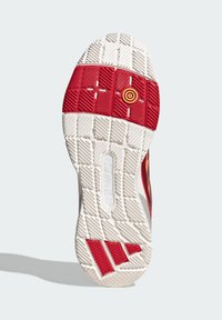 Podešev boty vyrobená z gumového materiálu; má texturovaný bílý základ, červené a bílé vzorované části a uprostřed oranžový kruhový detail.