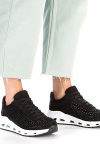 Baskets noires avec texture perforée, dotées d'une semelle intermédiaire blanche. Les lacets sont assortis au matériau supérieur, avec une conception de bout arrondi.