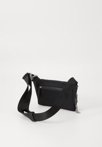 Bolso bandolera negro de tela con cierre de cremallera, correa ajustable y bolsillo frontal. Presenta una textura suave y accesorios de hardware en plata.
