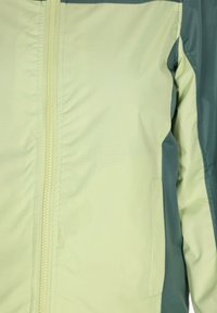 Ljusgrön jacka med dragkedja framtill, mörkgrön övre del och sidfickor. Har en slät tygtextur och en hållbar design.