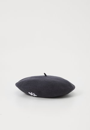 Sort uldberet med en lille topstamme og hvide broderede initialer på siden, placeret på en hvid overflade.