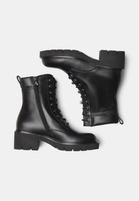 Bottines en cuir noir avec une semelle épaisse, dotées d'une fermeture éclair sur le côté, d'un laçage à l'avant avec œillets en métal, et d'une finition texturée.