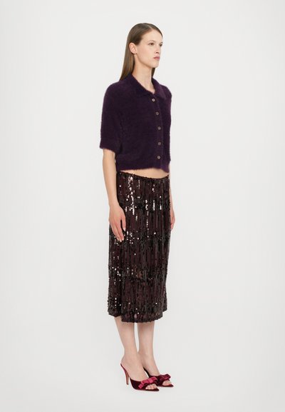 Lila, flauschige, kurz geschnittene Strickjacke mit kurzen Ärmeln, kombiniert mit einem mit Pailletten besetzten braunen Rock mit geschichtetem Fransen und burgunderfarbenen, hochhackigen Sandalen.