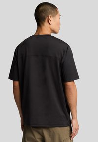 T-shirt nera a maniche corte con una vestibilità rilassata, texture liscia, dettagli di cucitura minimi lungo la schiena e scollatura arrotondata.