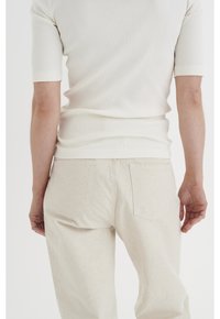 Tight ribbat vit topp som är kombinerad med löst sittande, ljusbeige byxor med bakfickor och en strukturerad tyg.