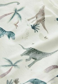 Hellfarbiger Stoff mit einem Dinosauriermuster in verschiedenen Farben, darunter Grün, Braun und Grau, mit Akzenten von Palmen und einer weichen Textur.