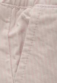 Ljusrosa tyg med subtila vertikala ränder, med texturerad yta och sömnadsdetaljer, som visar en prydlig vikning vid kanten.